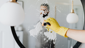 Persoon reinigt spiegel met spons en gele handschoenen — schoonmaakmiddelen gids Eco-Box.NL
