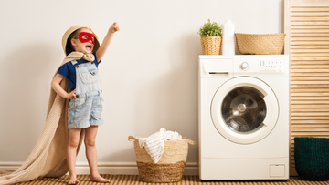 Kind in een superheldenoutfit staat trots naast een wasmachine, symbool voor veilig en natuurlijk schoonmaken met Eco‑Box.